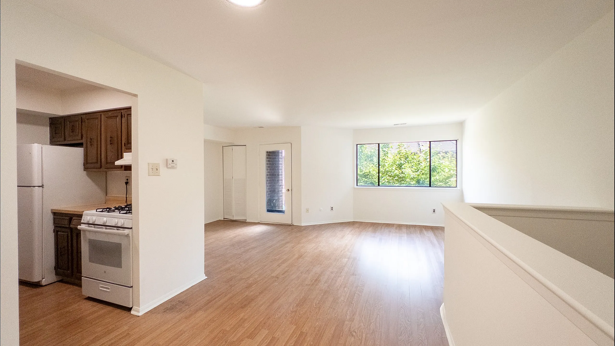 Bright open-plan living space with wooden flooring, featuring a cozy kitchen and large windows with garden views.