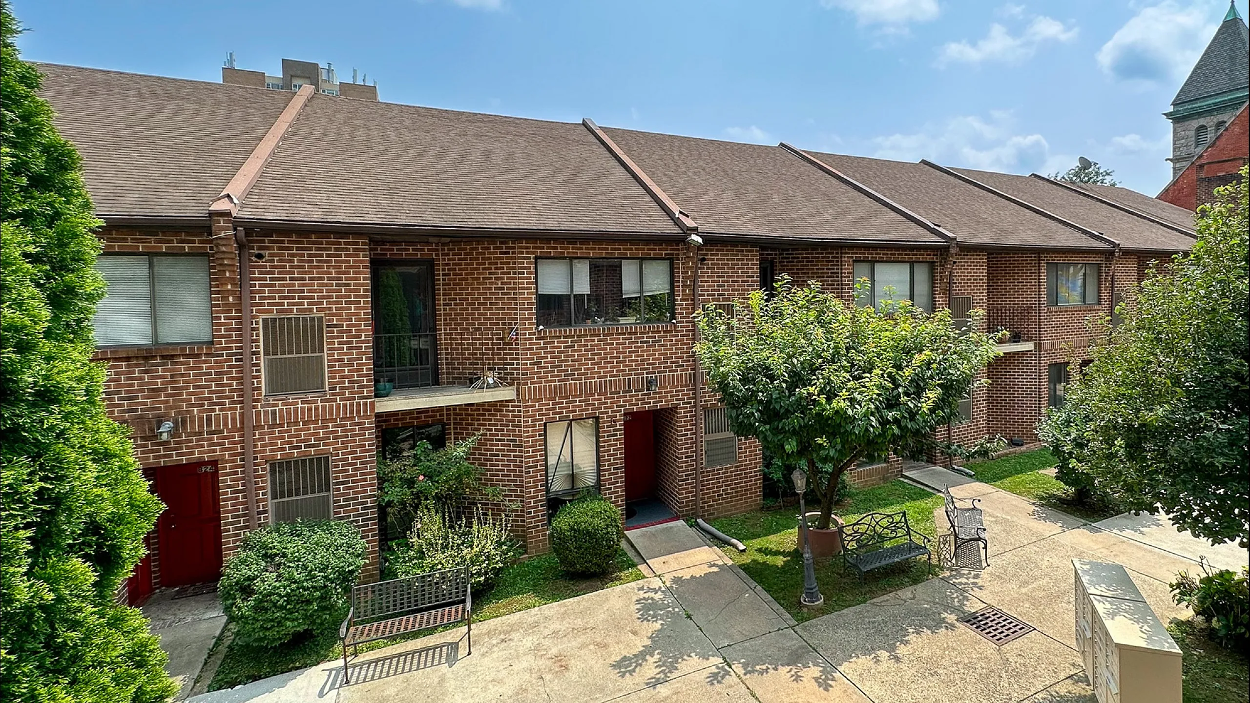 Charming red brick apartment complex with lush greenery and inviting outdoor seating in a serene courtyard.