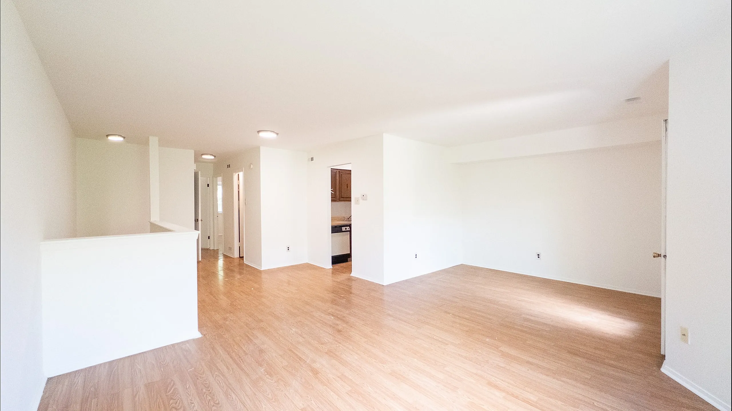 Bright and spacious open-plan living room with hardwood flooring, featuring modern recessed lighting and a view into the stylish kitchen.