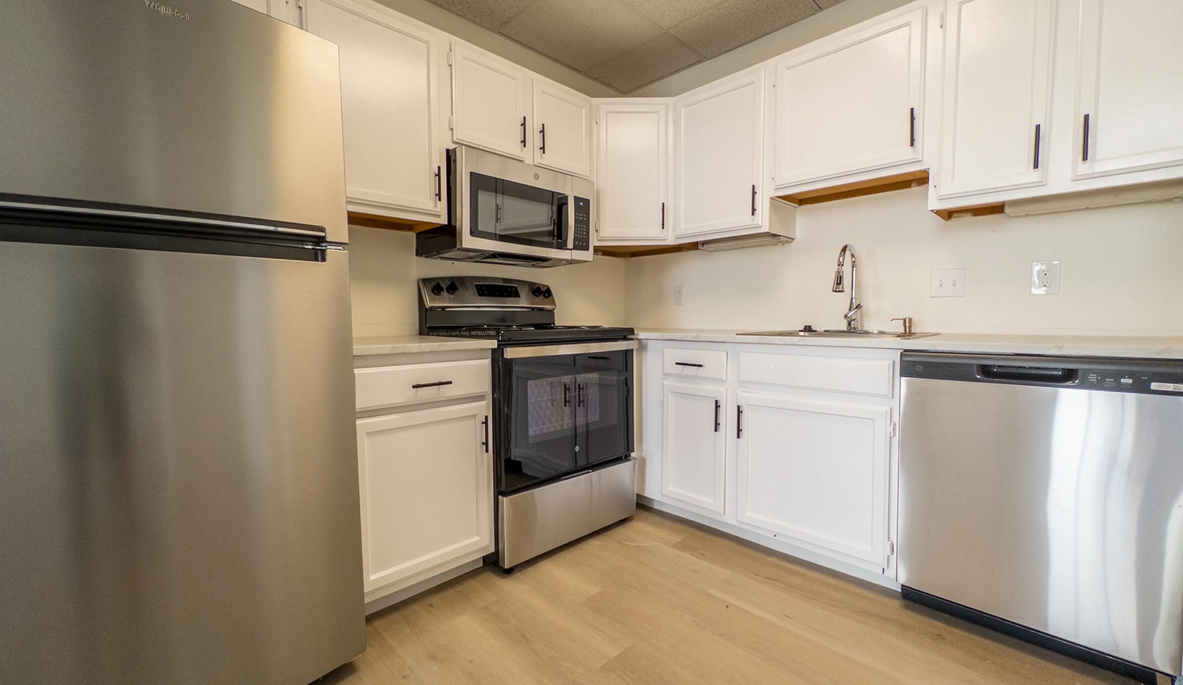 Chic modern kitchen with sleek stainless steel appliances, white cabinetry, and elegant hardwood floors.
