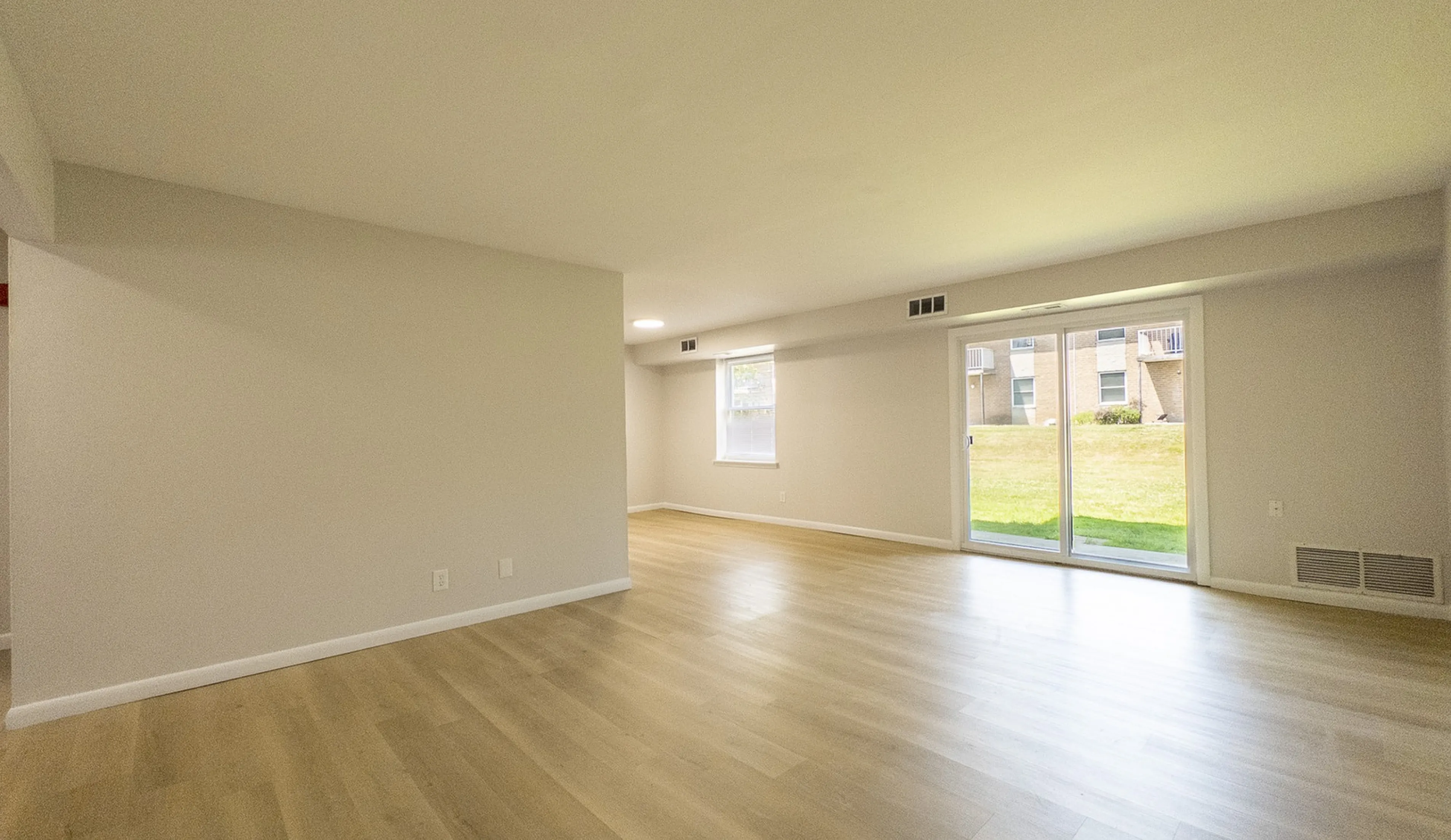 Spacious and inviting living room with elegant wood flooring, large windows, and sliding glass doors providing abundant natural light and easy access to a green outdoor space.