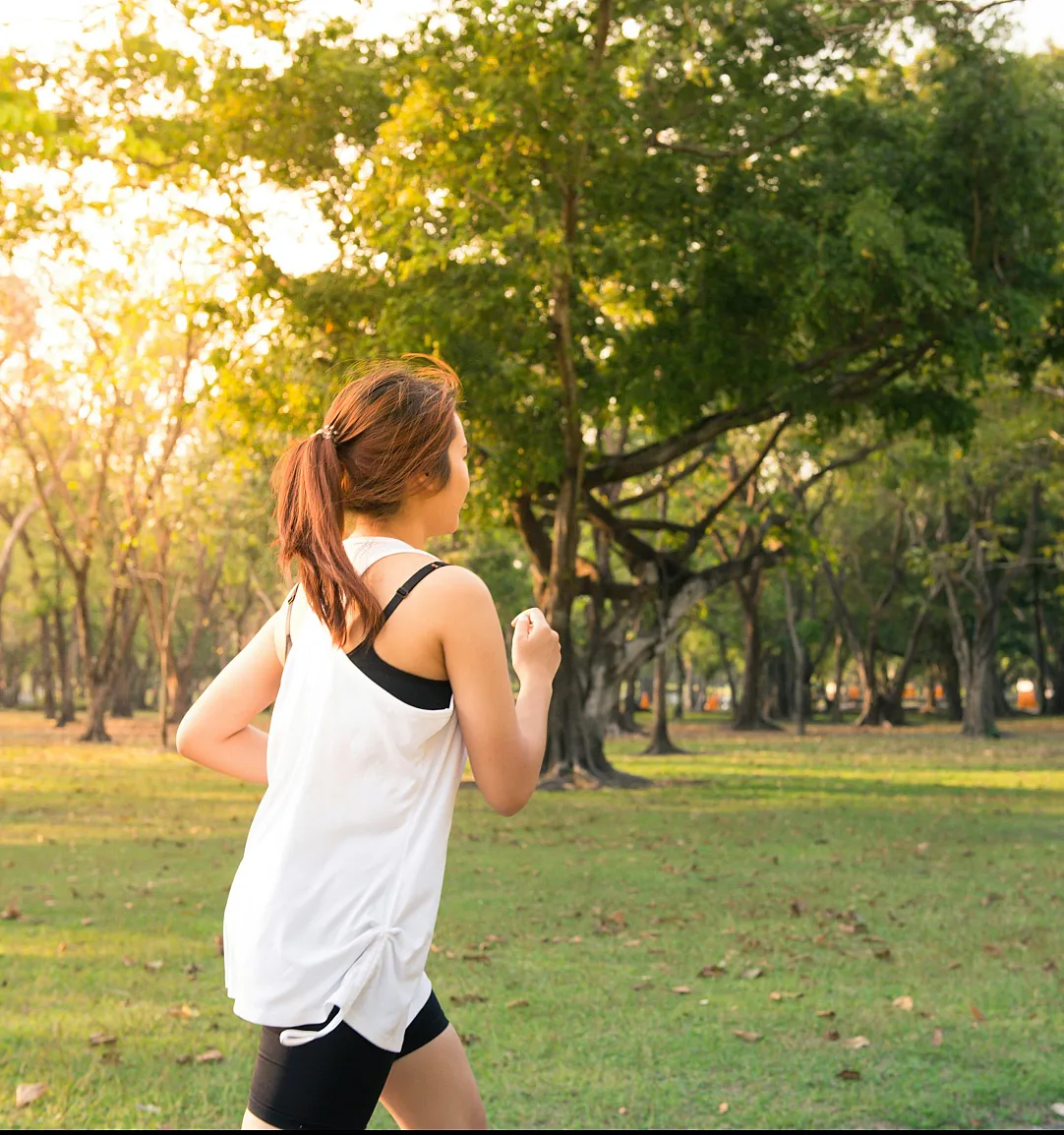 woman running in a green, sunny park with trees
