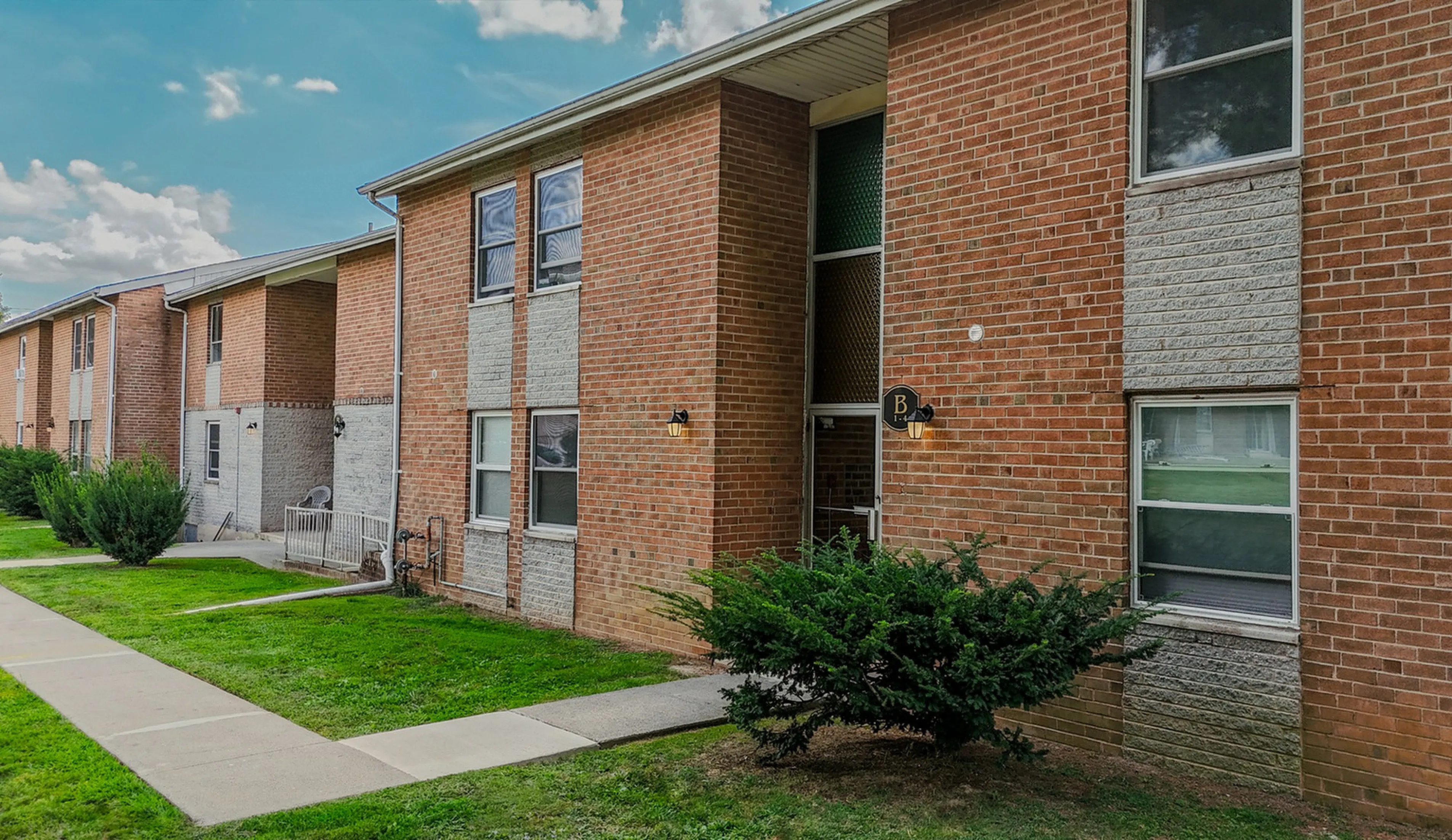 Charming brick apartment building with modern windows and lush green surroundings, offering a welcoming and cozy atmosphere.