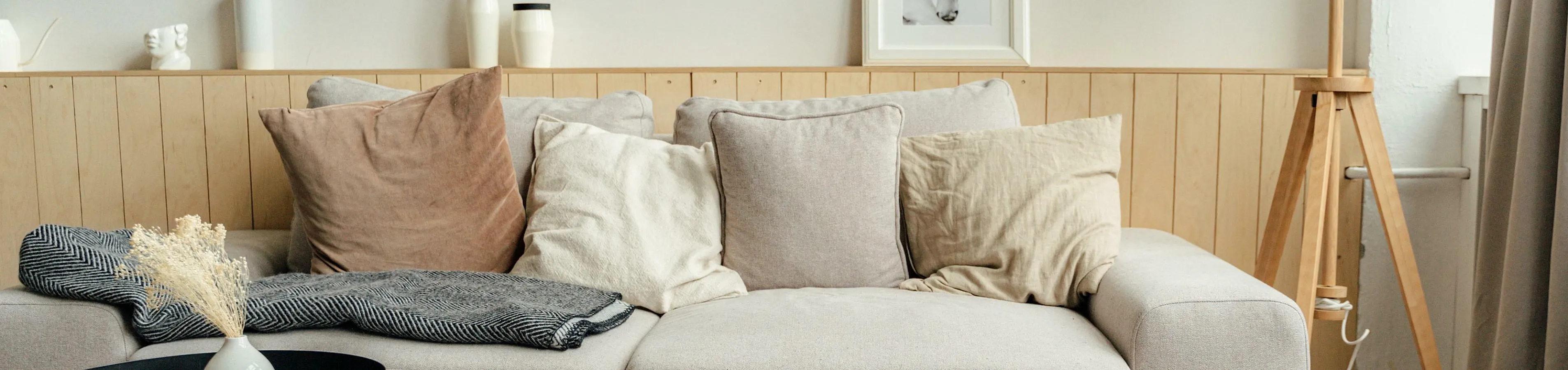 Cozy living room with a stylish beige sofa, accent pillows, modern floor lamp, and a chic coffee table atop a textured rug.