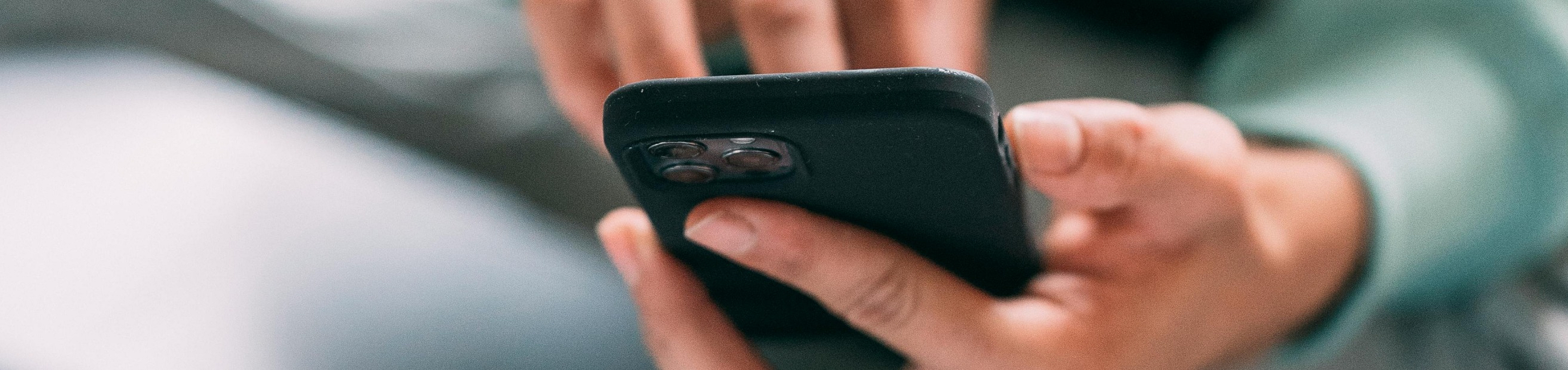 Close-up of a person using a smartphone, dressed in casual clothing and seated comfortably with a laptop nearby.
