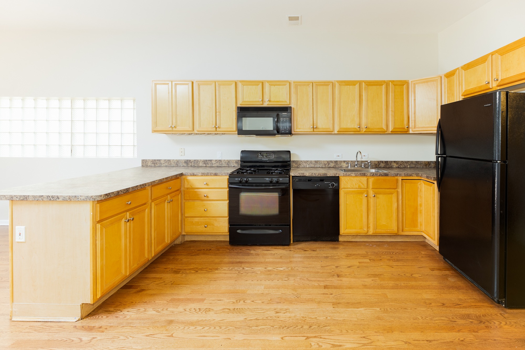 Open concept kitchen layout with a light wood cabinets, black appliances, and light hardwood floors.
