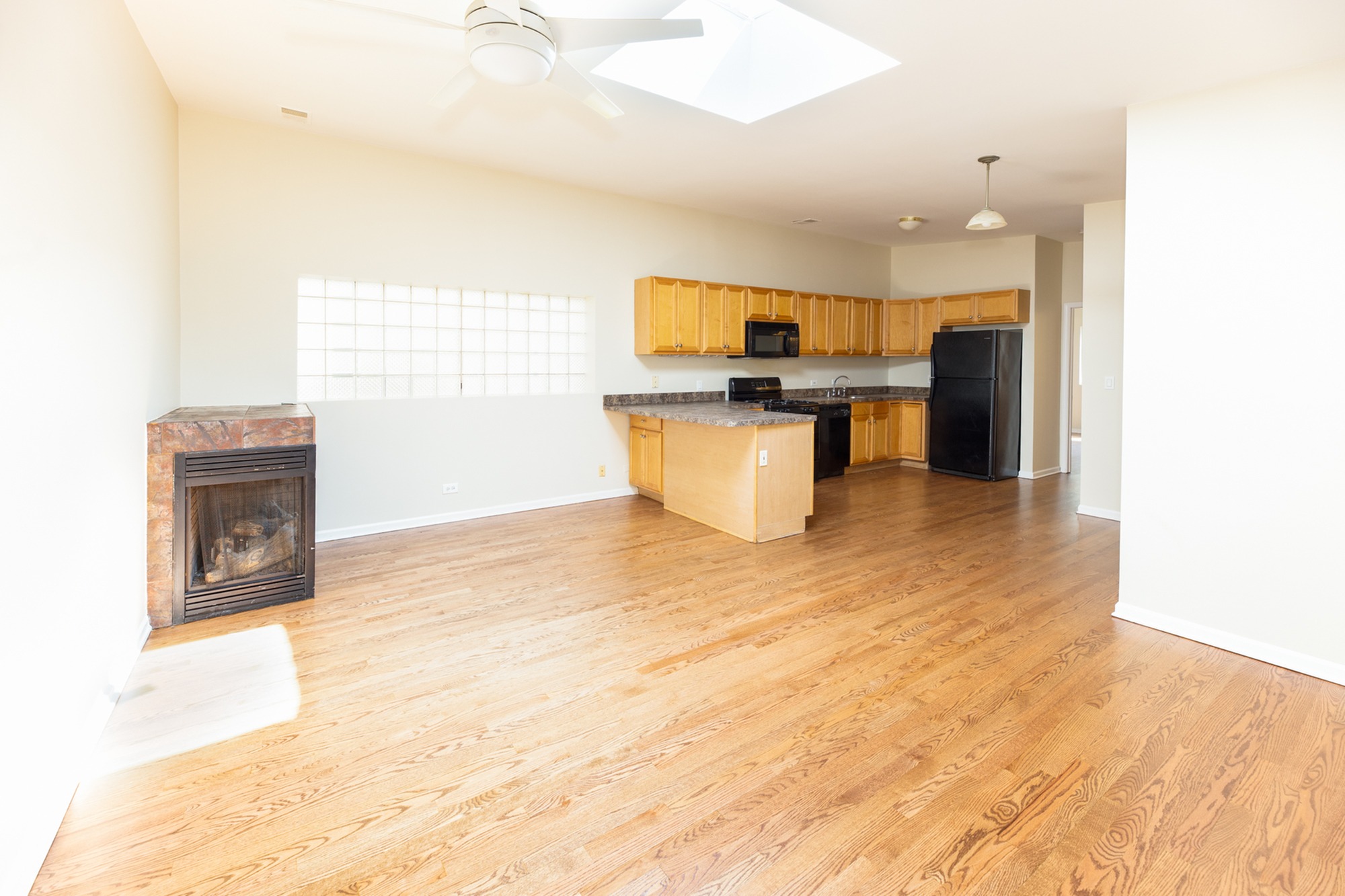 Kitchen / living room combo with a fireplace, light hardwood floors, a skylight, and a ceiling fan.
