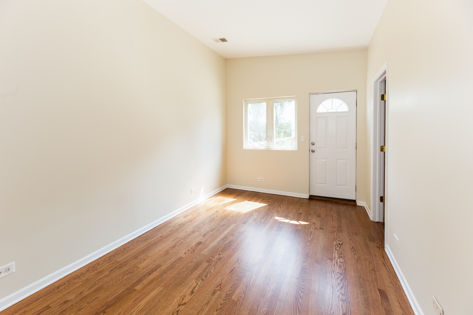 A bedroom with hardwood floors, and off white walls with white trim..