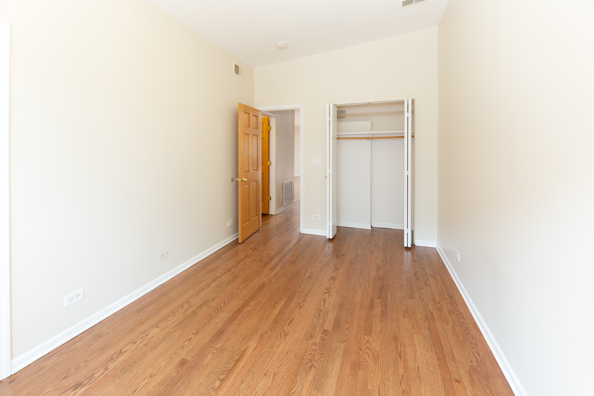 A bedroom with good closet space and medium toned hardwood floors.