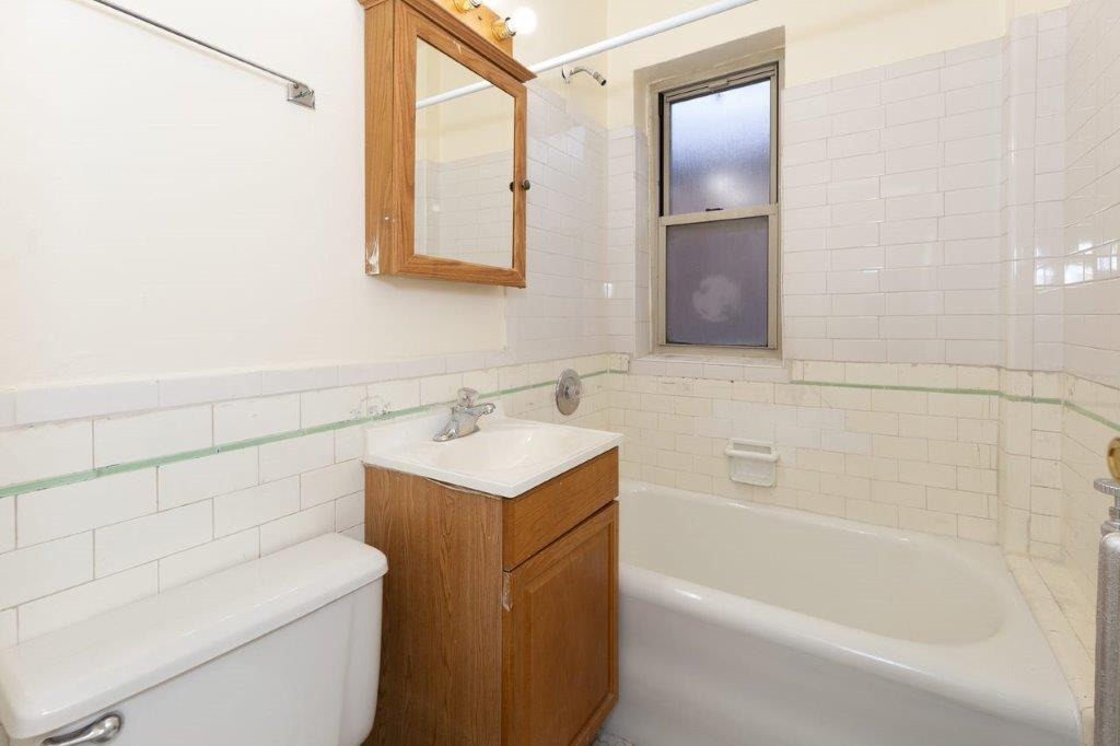 Apartment 107 Bathroom with wooden vanity and white bathtub.