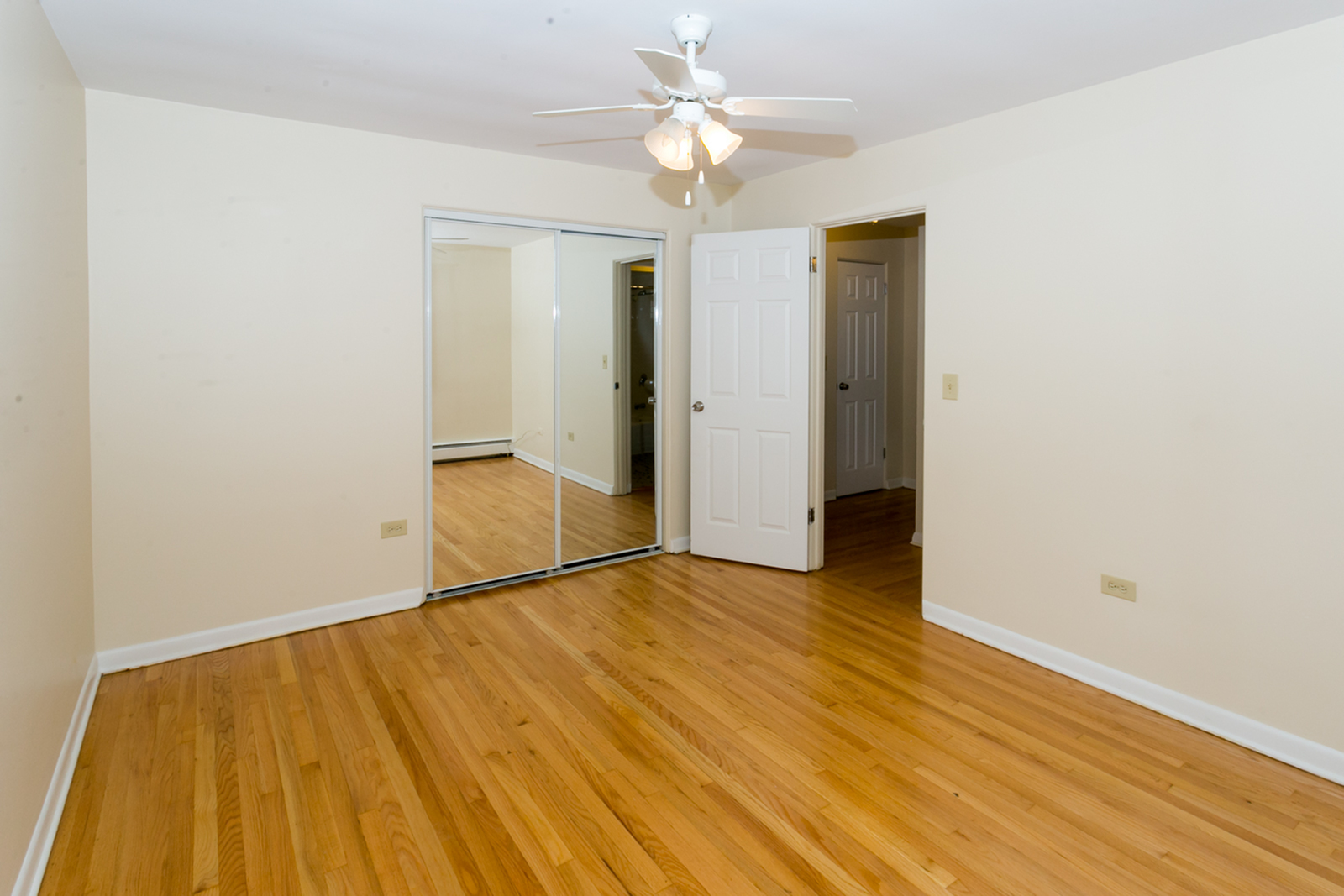 Bedroom with hardwood floors mirrored closet door and ceiling fan.