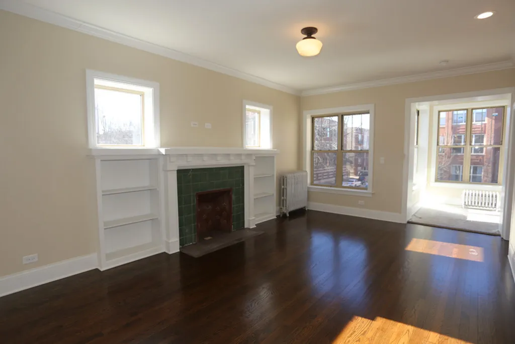 Living room looking into the sun room.  Hardwood floors and a decorative fireplace with bookshelves are featured.