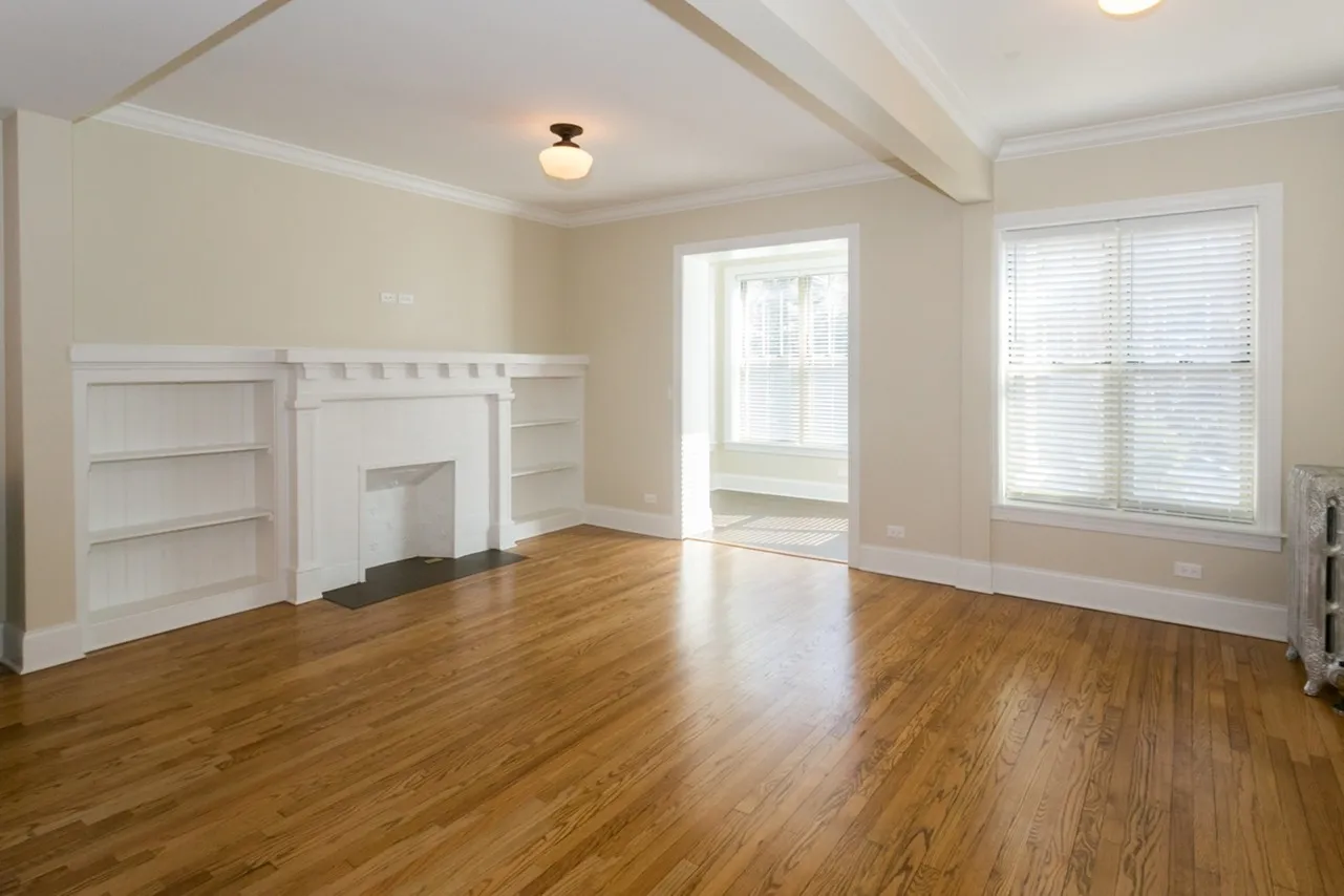 A living room with light hardwood floors, a decorative fireplace, sunny windows, and a schoolhouse ceiling light fixture..