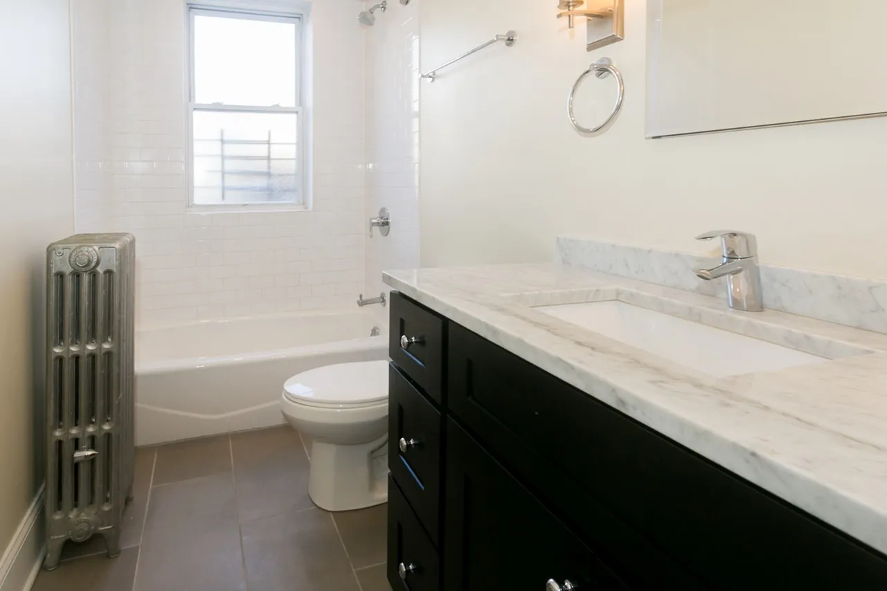 A remodeled bathroom with an ebony vanity, grey granite countertop, and dark grey tile floors.