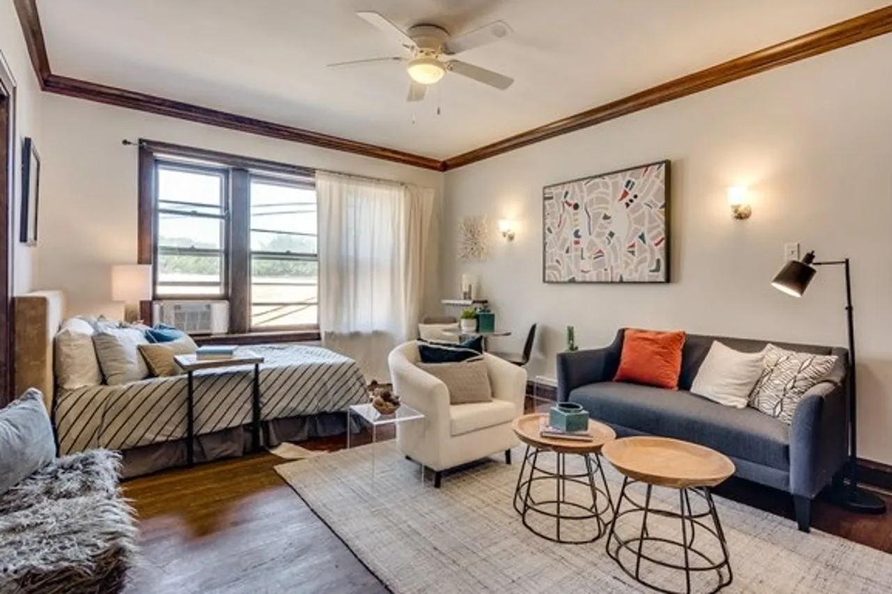 A large model studio apartment with hardwood floors, off white walls, natural wood trim, and a ceiling fan.