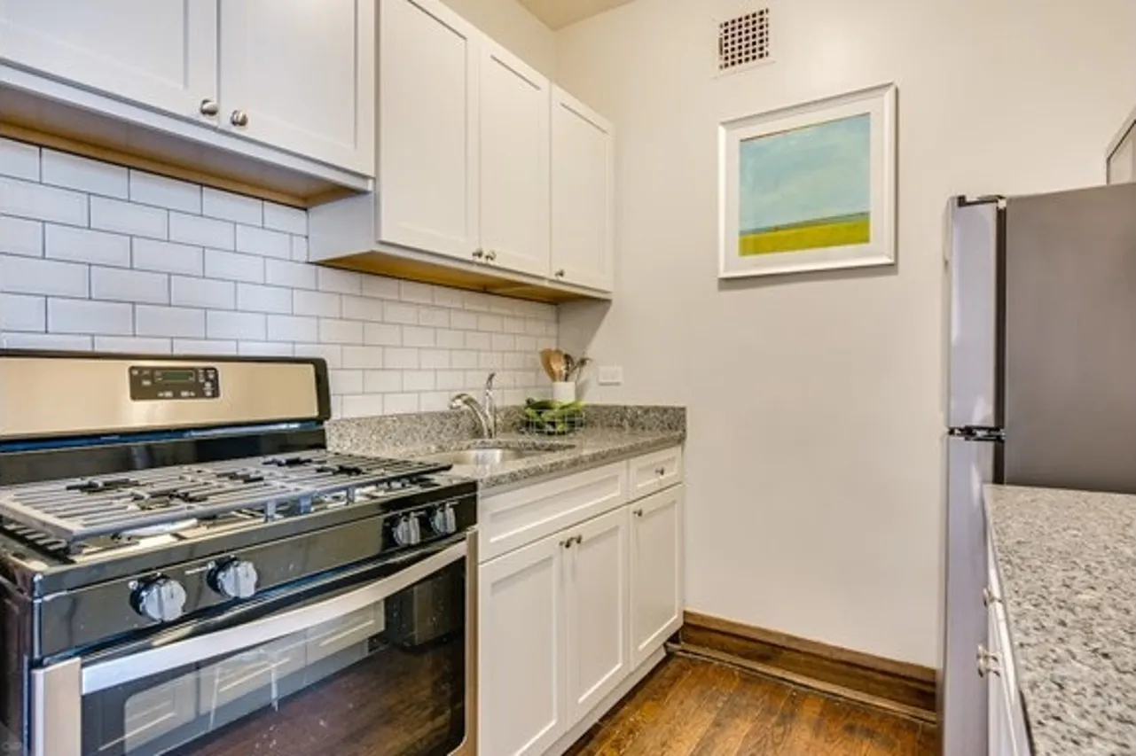 A separate and upgraded kitchen with white cabinets, grey granite countertops, and stainless steel appliances.