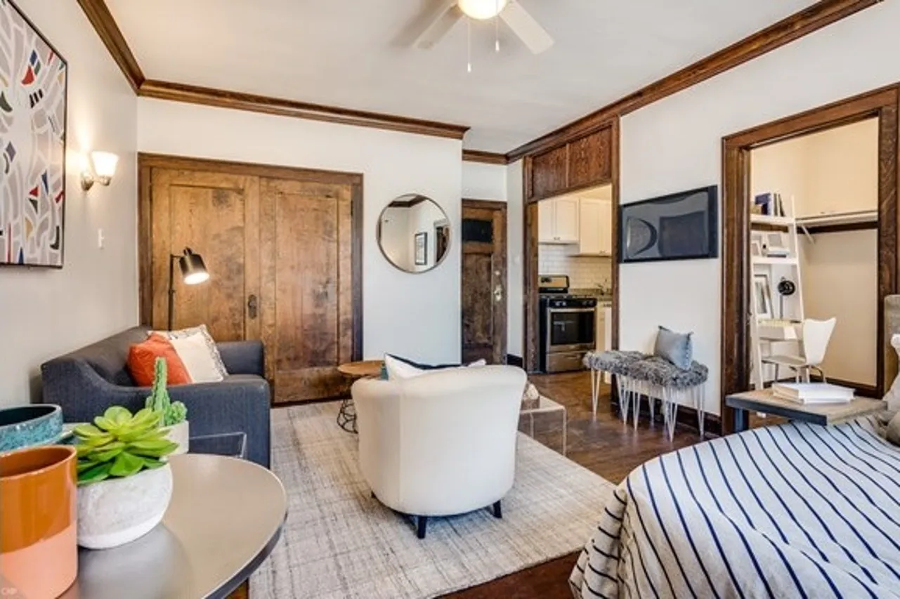 Living space decorated with stuffed furniture and a beige rug.  Walls are off white and trim is natural wood.