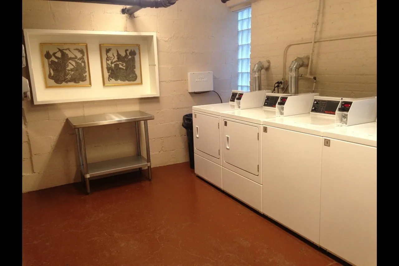 The laundry room with coinless machines, a folding table, and framed Asian art.
