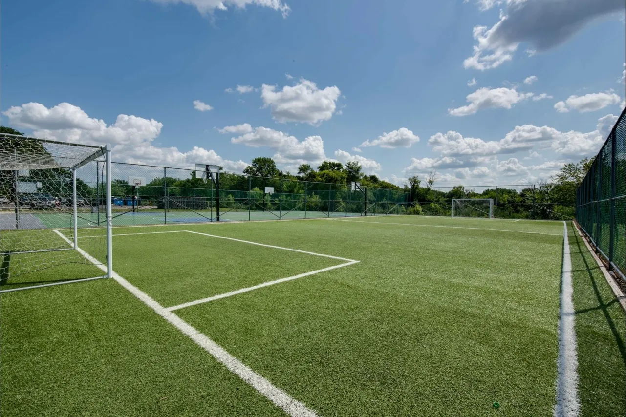 Kids soccer field with bright green grass under fluffy white clouds on a summer day.
