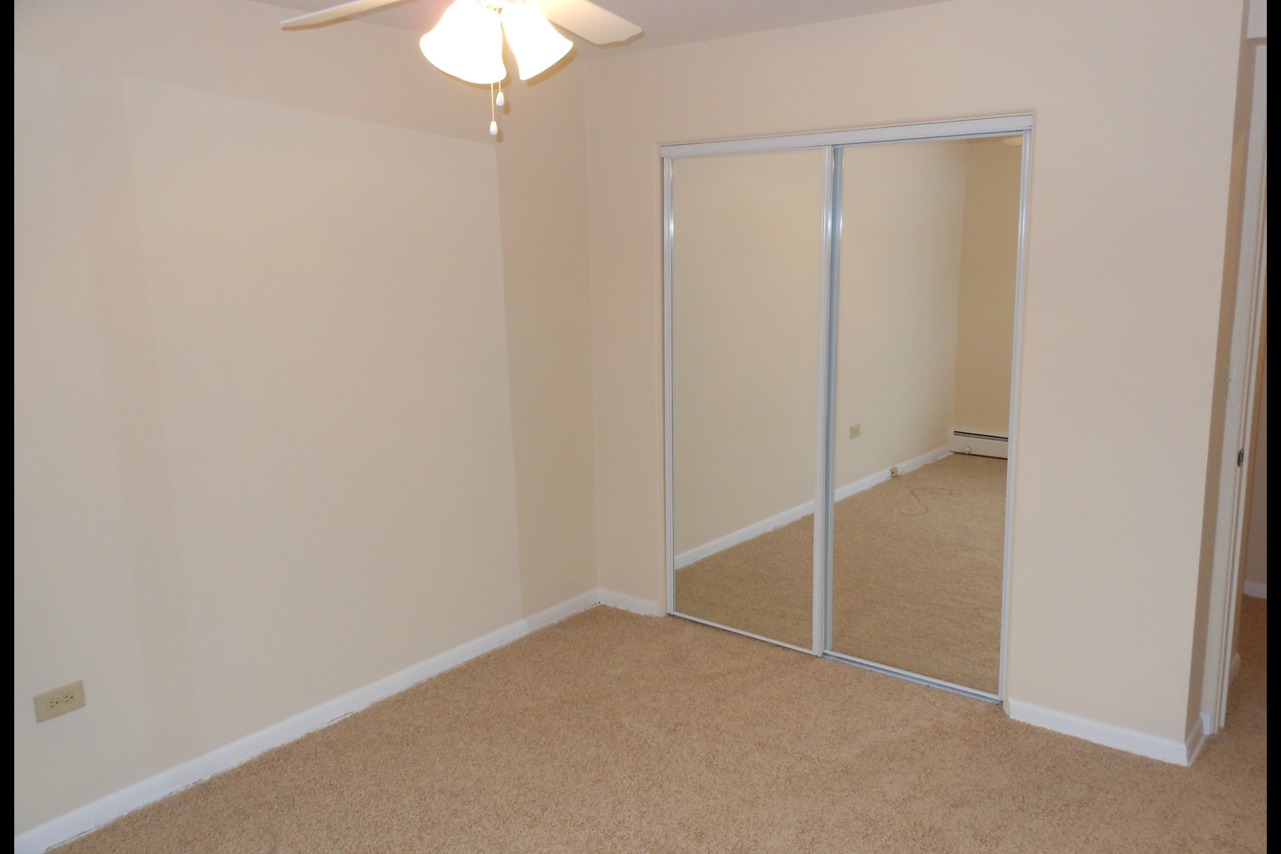 Carpeted bedroom with mirrored closet doors and a ceiling fan.