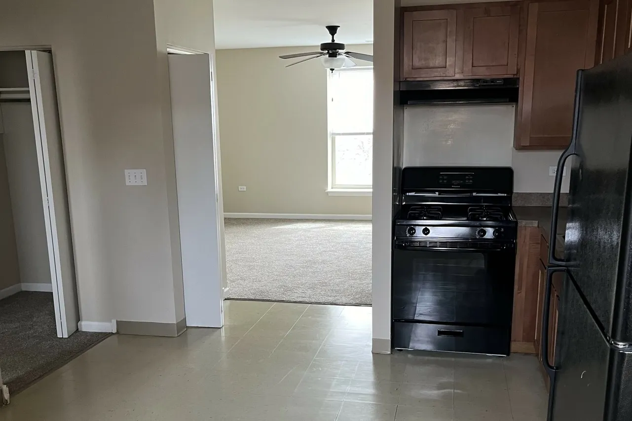 A kitchen with tile flooring and black appliances looking into the carpeted living room.