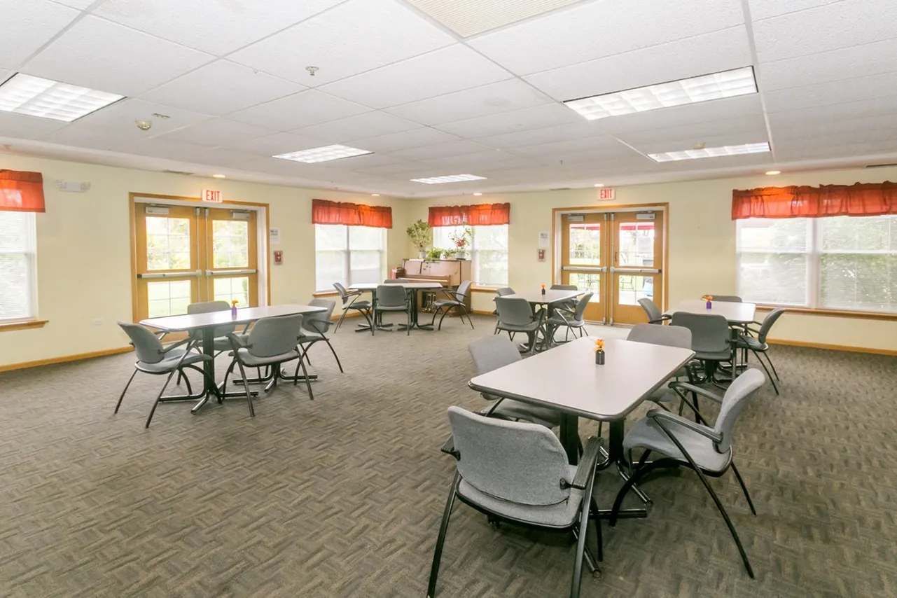 Community room with sunny windows, and numerous tables and chairs.
