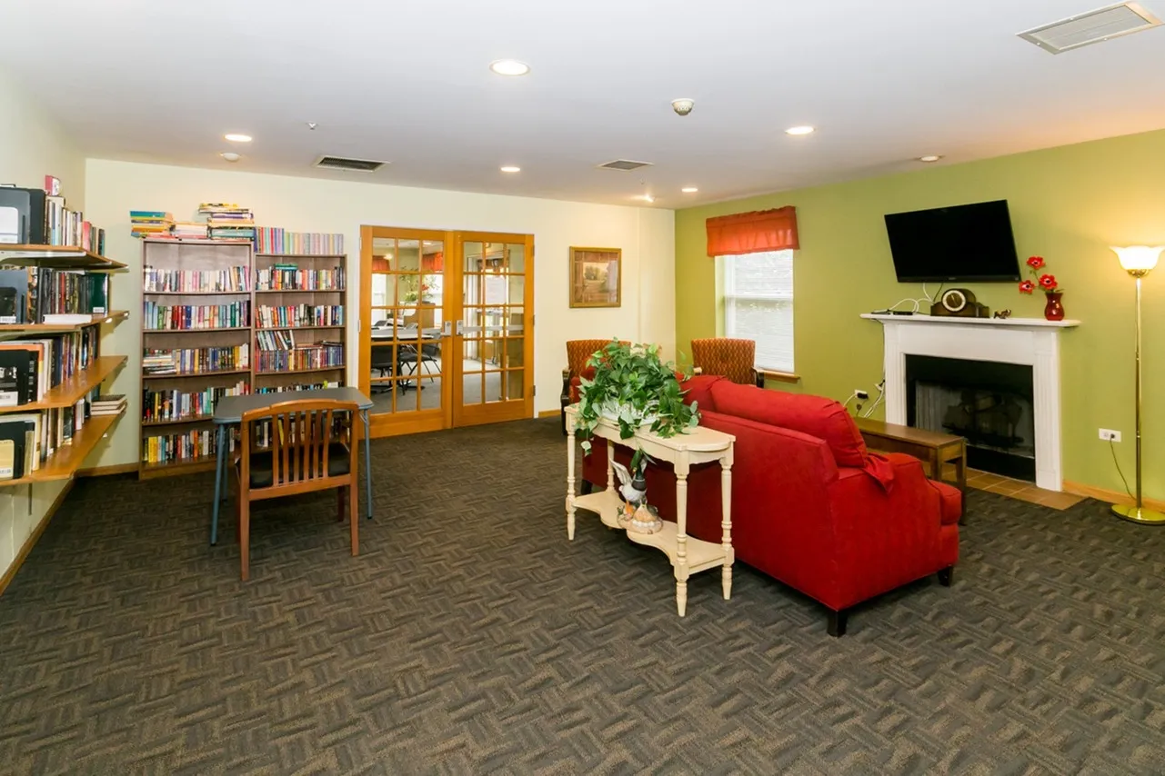 Nicely appointed community space with figured carpeting, stuffed furniture, a television, and a fireplace.
