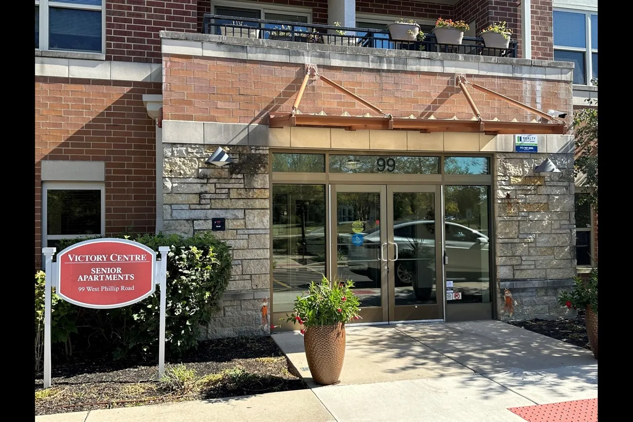 Exterior entrance to Victory Centre Senior Apartments of Vernon Hills with a planter in front glass doors.