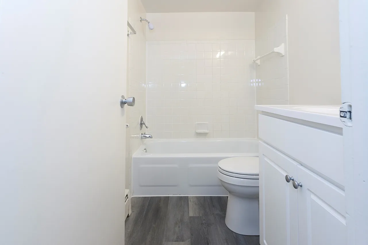 A bathroom with white vanity, white tiles surrounding a bathtub, and a dark grey floor.