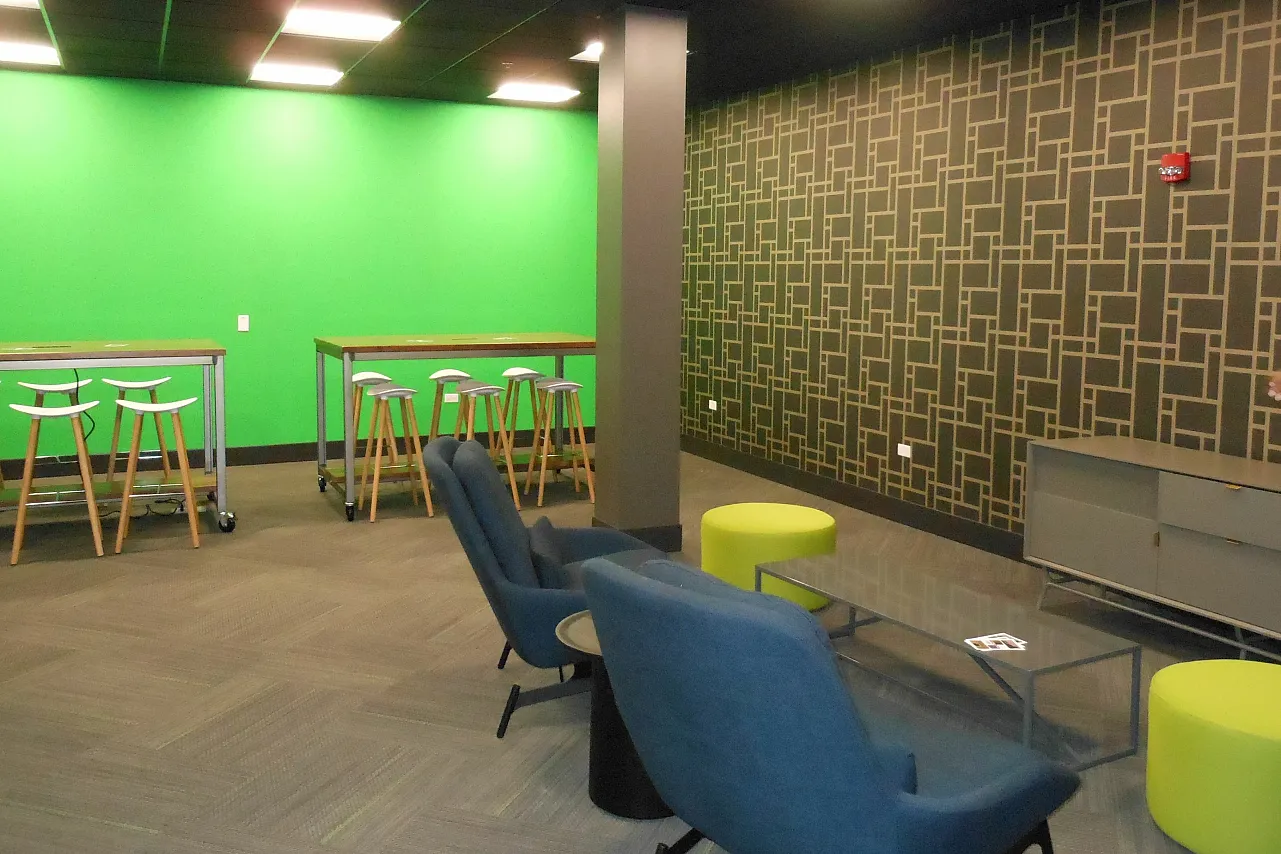 A lounge area with soft lighting, chairs and a community table for residents to enjoy.