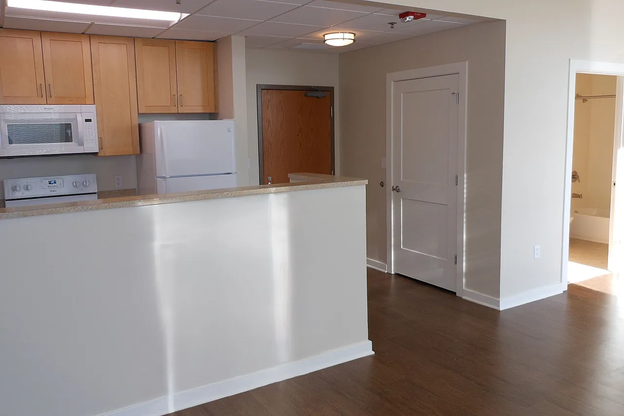 An open kitchen in some units with white appliances and wooden cabinets.