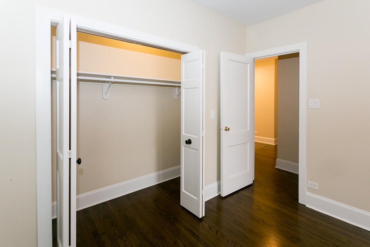 A big closet space in a bedroom with dark hardwood floors, and off white walls with white trim.