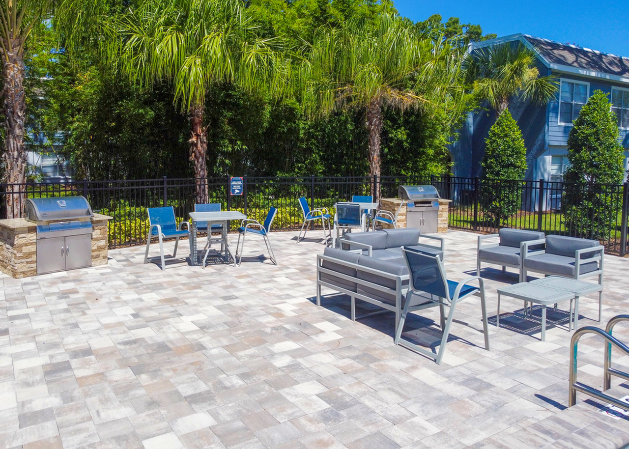 Pool griling area with grill, gray cushioned patio furniture, blue chairs and gray tables