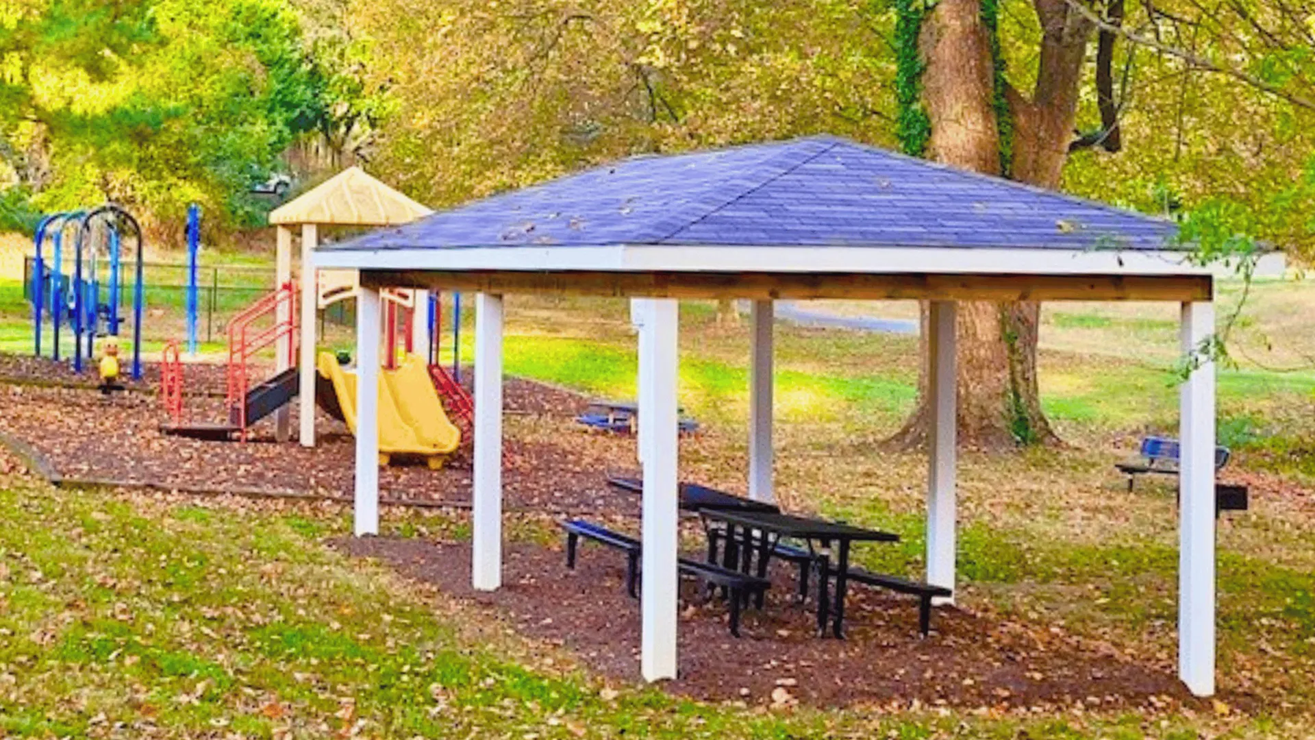 Charming outdoor playground with vibrant slides and swings nestled under lush trees, featuring a cozy picnic pavilion.