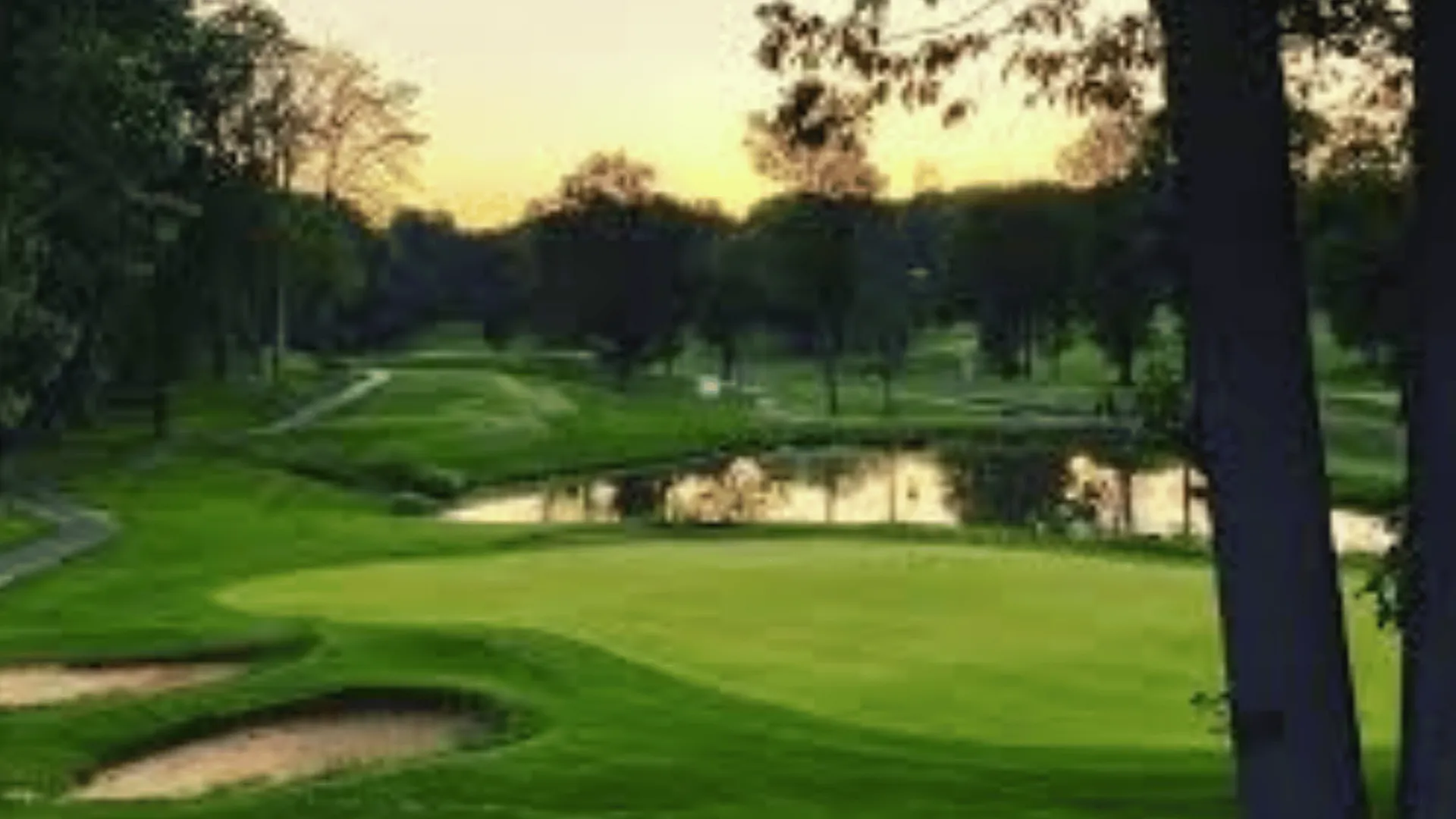Idyllic golf course view at sunset featuring lush greenery, serene water features, and scenic walking paths.