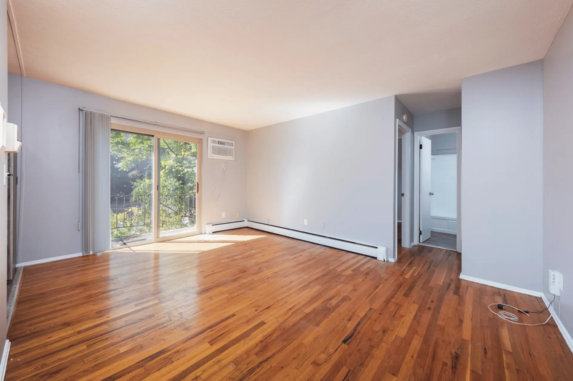 Spacious living room with hardwood floors, large windows, and a view of greenery.