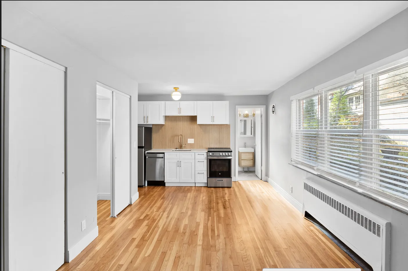Bright and modern kitchen with sleek white cabinetry, stainless steel appliances, and warm hardwood floors, featuring large windows for natural light.