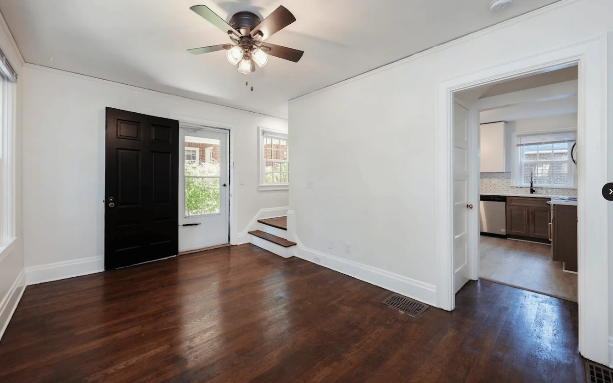 Bright living space with rich hardwood floors and an inviting ceiling fan, leading into a modern kitchen with sleek cabinetry.