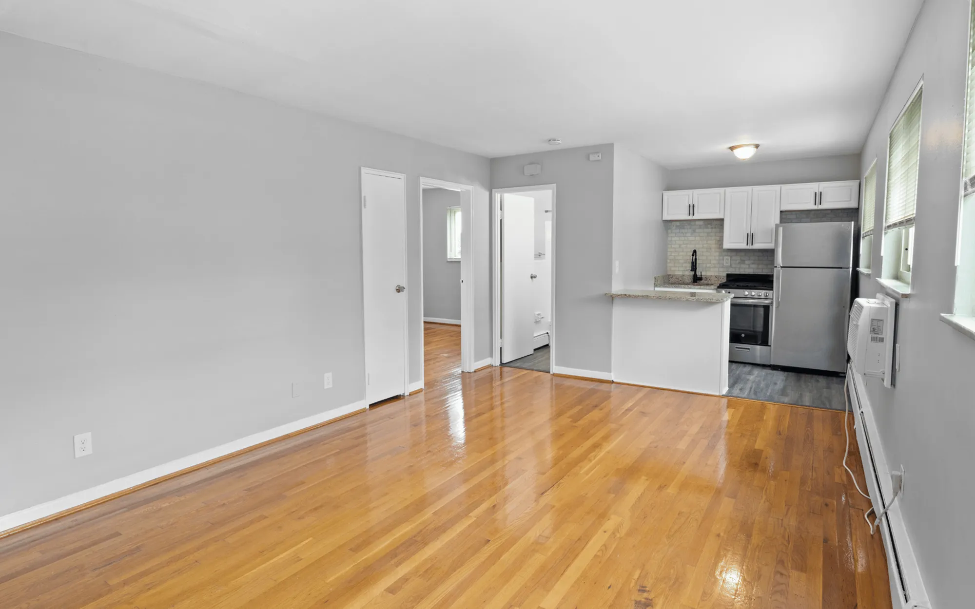 Modern apartment featuring an open floor plan with sleek hardwood floors, a stylish kitchen with stainless steel appliances, and abundant natural light through large windows.