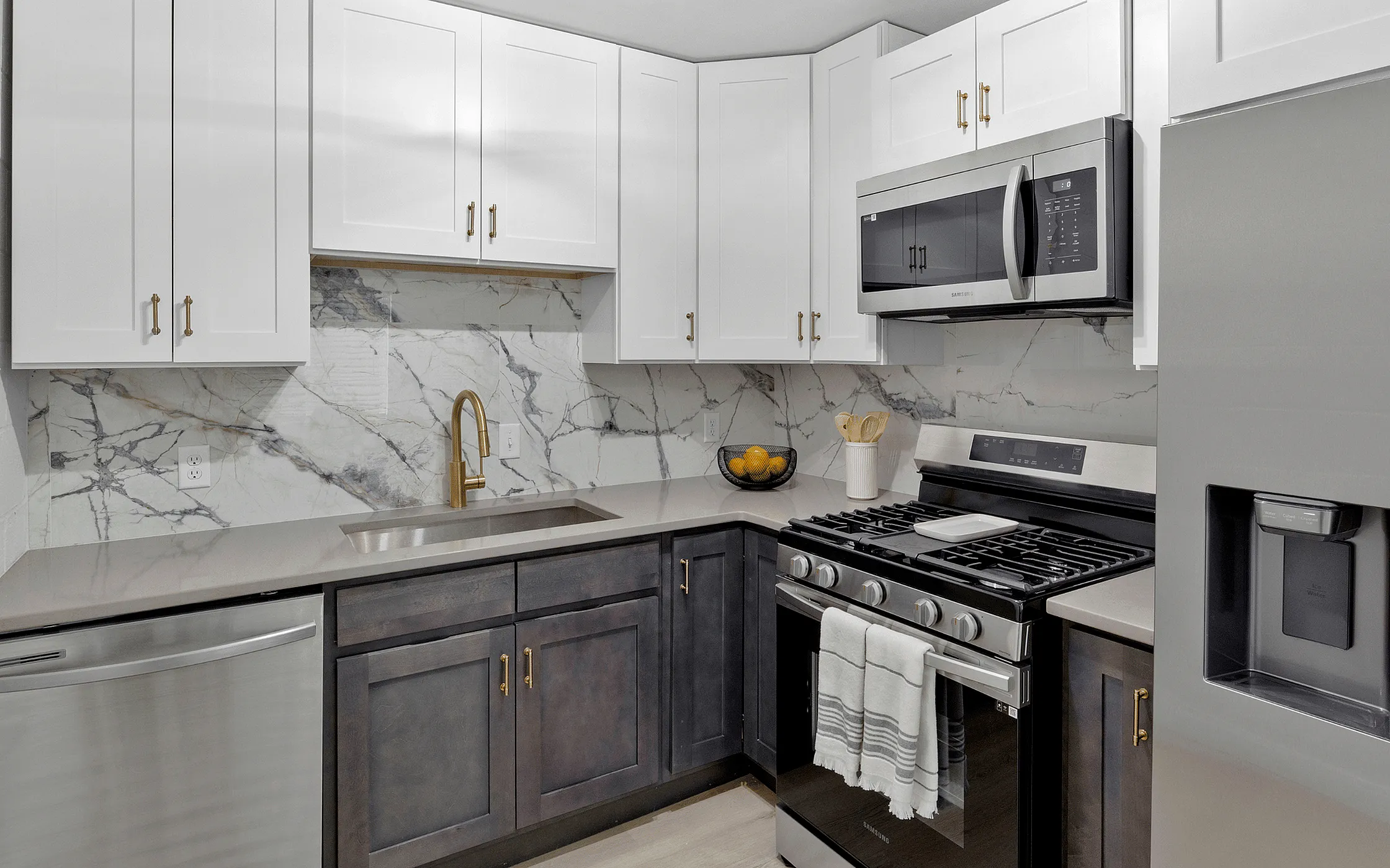 Modern kitchen with sleek marble backsplash, stainless steel appliances, and contrasting white and dark cabinetry. Elegant gold faucet complements the sophisticated design.