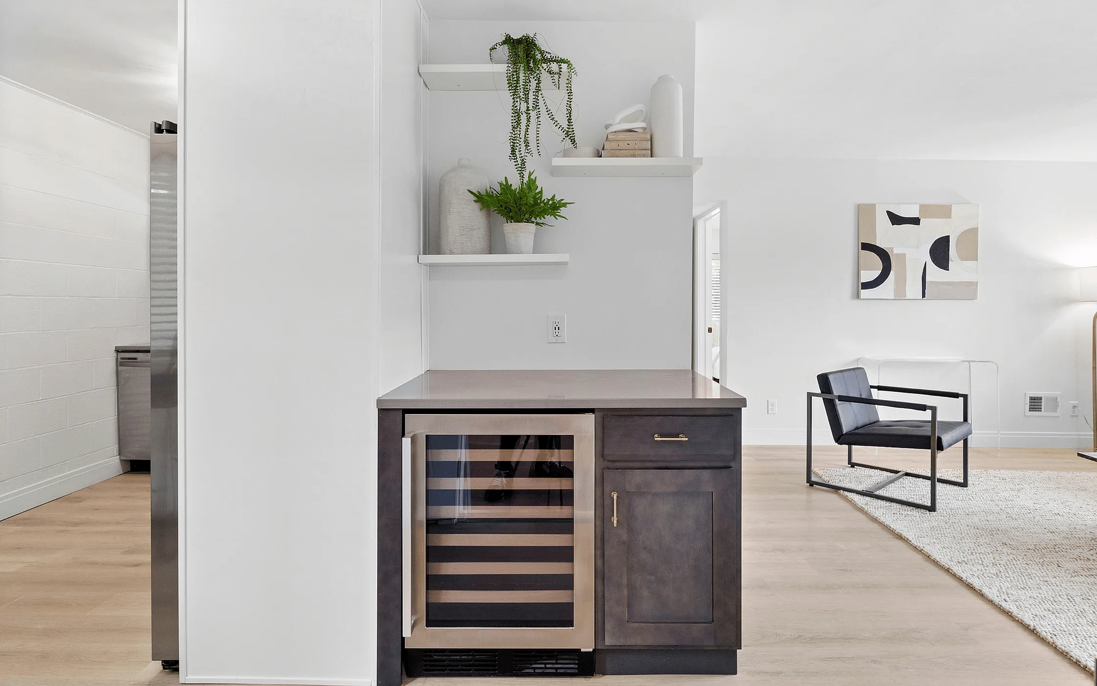 Modern living space featuring sleek wine cooler, open shelving with decorative plants, and stylish armchair in a minimalist setting.