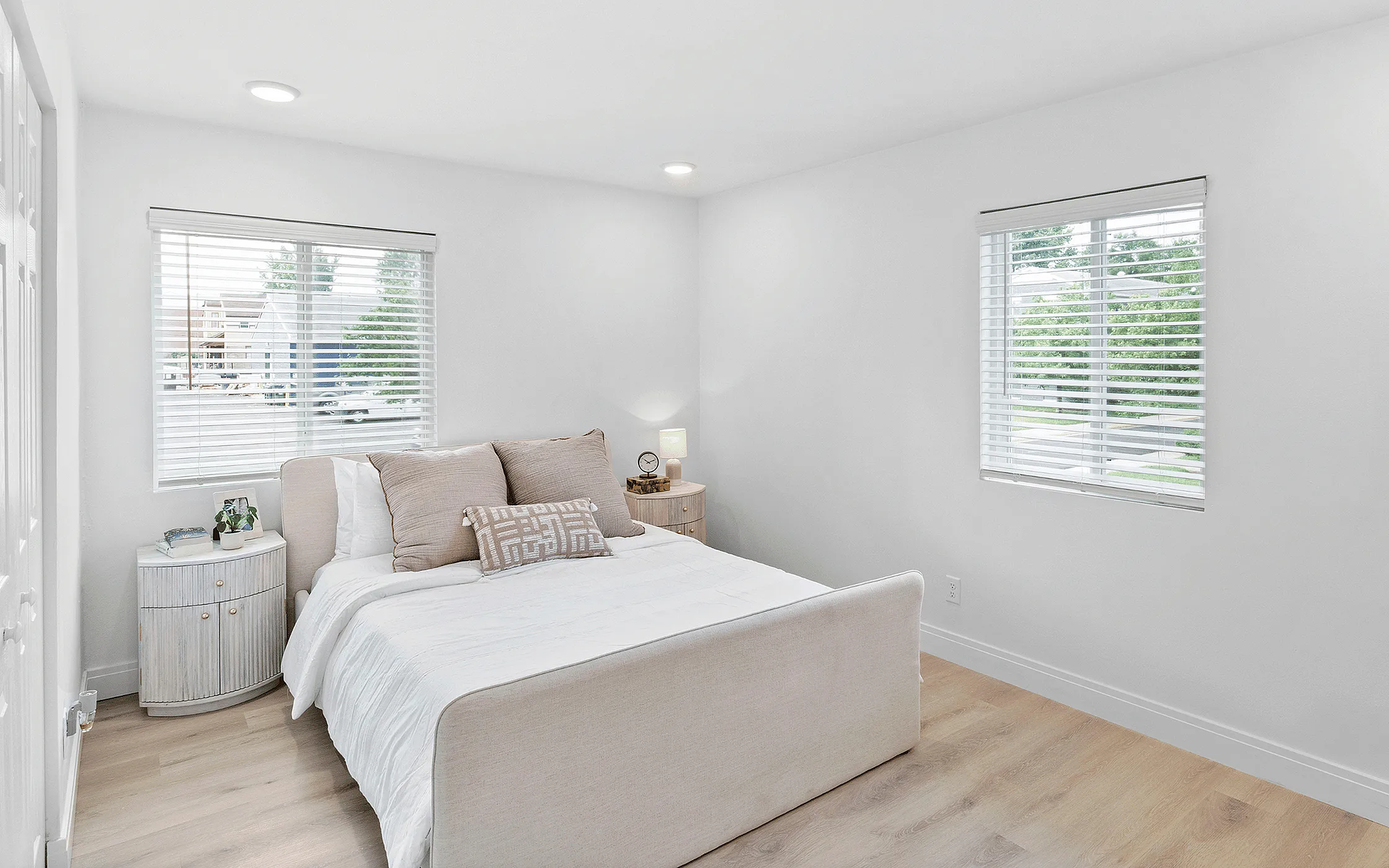 Bright and airy bedroom with modern decor, featuring a comfortable bed and stylish side tables. Natural light fills the room through large windows with blinds, creating a serene and inviting atmosphere.