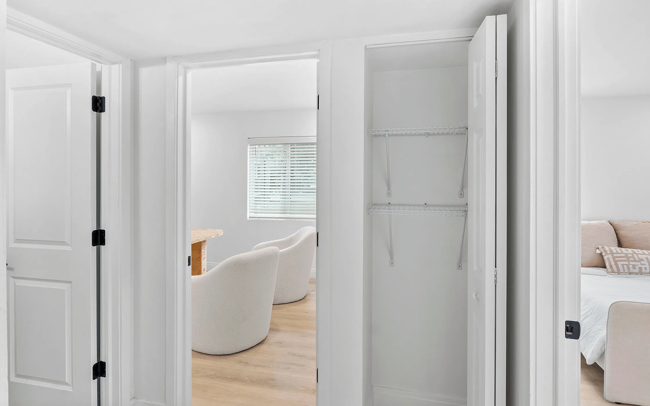 Bright and inviting hallway view with a cozy living space, featuring plush chairs, large windows, and a neatly organized closet.