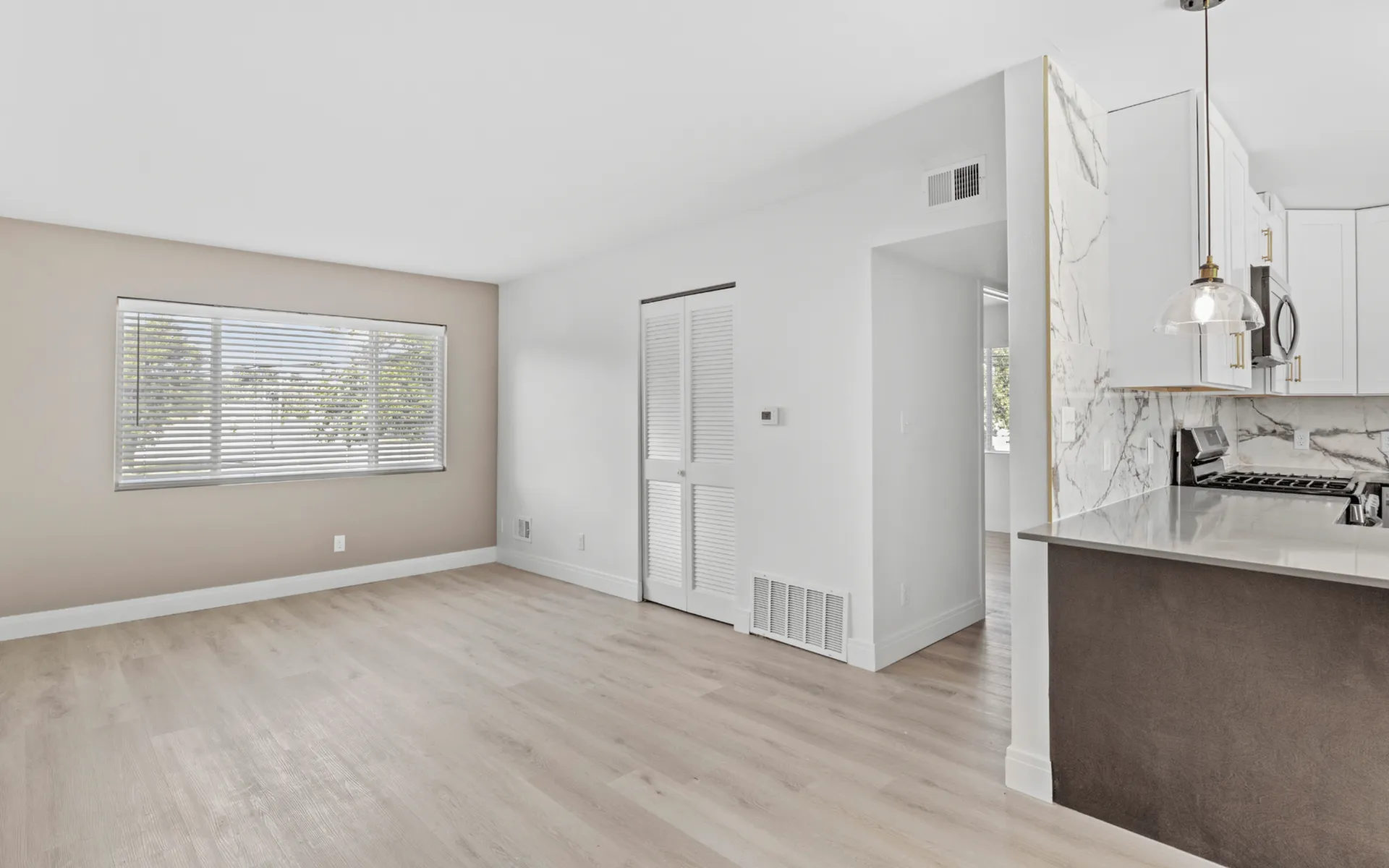 Bright living space with fresh hardwood floors, large window, and modern kitchen with marble accents.