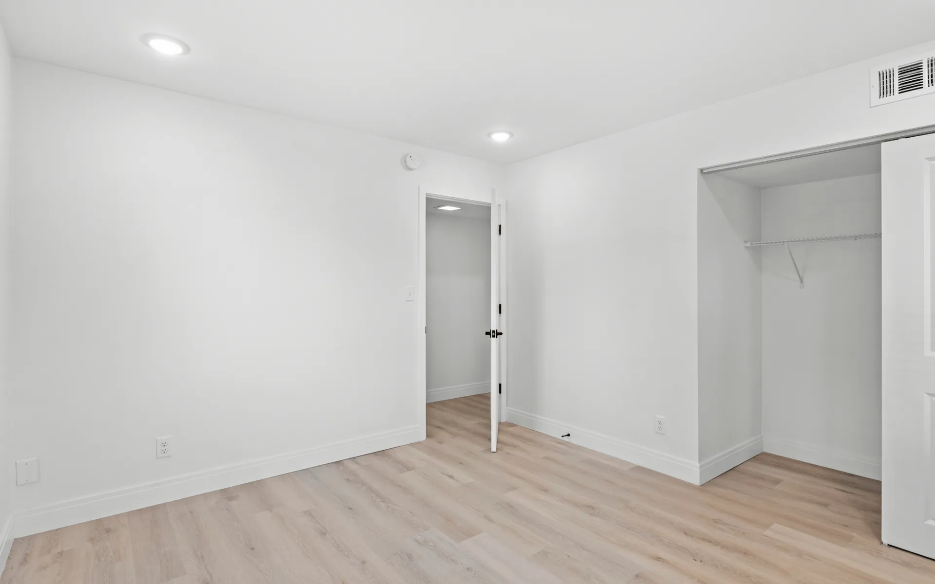 Bright and airy room with sleek white walls, modern closet, and elegant wood flooring, ideal for a personalized living space.