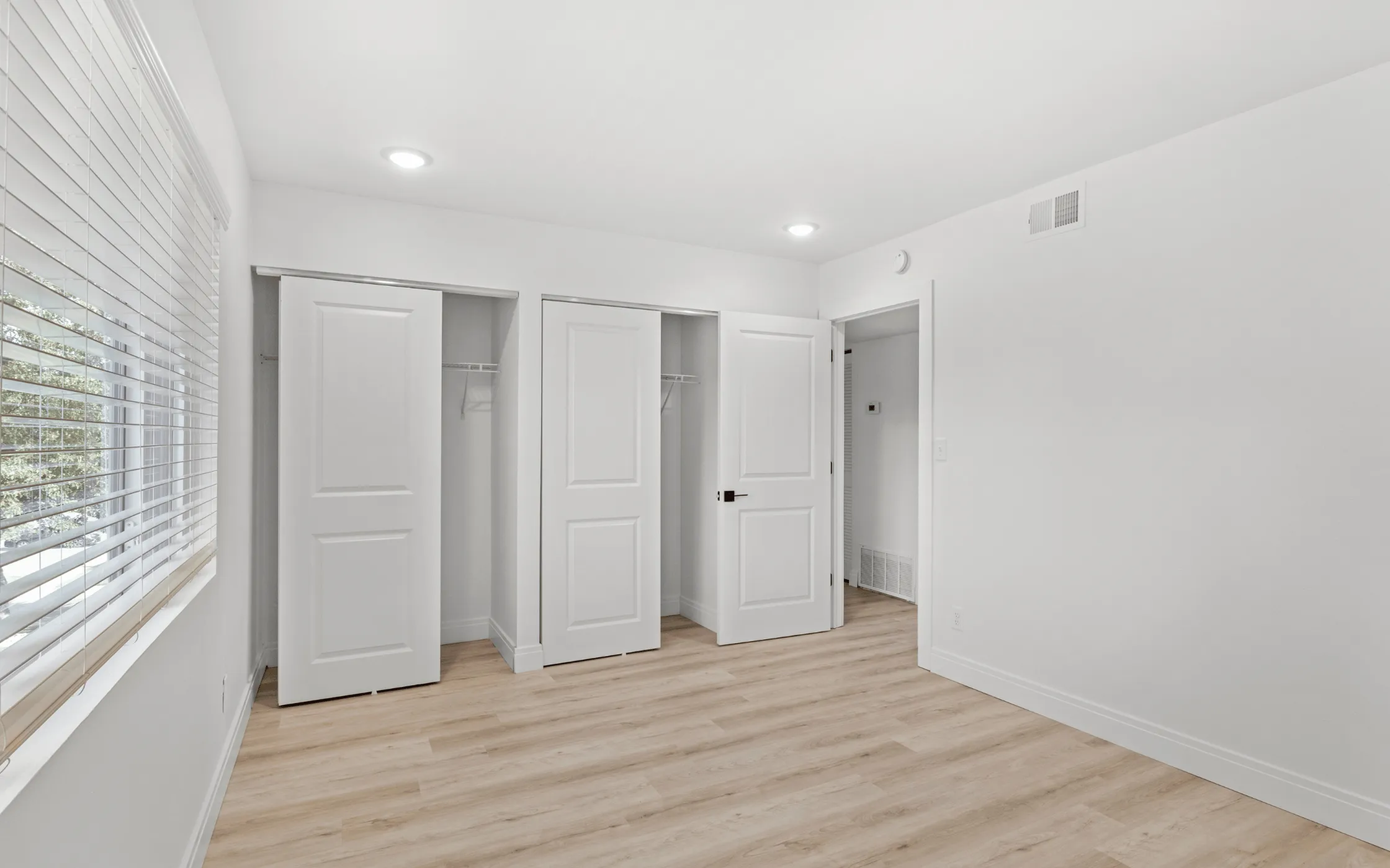 Bright and modern bedroom with large closet space, white walls, and natural light through wide windows.