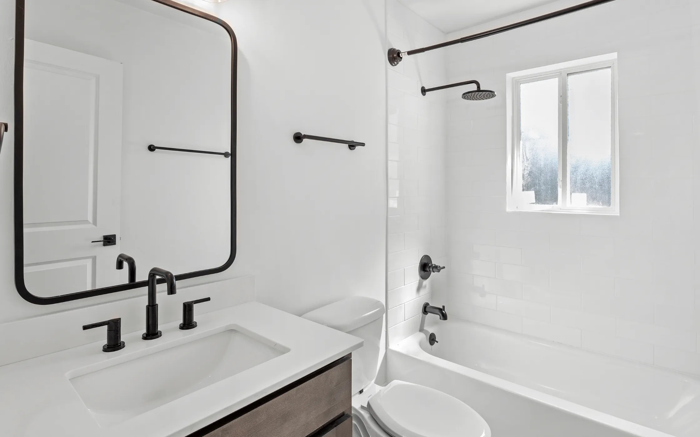 Elegant bathroom featuring a modern white countertop, sleek black fixtures, and a spacious bathtub under natural light.