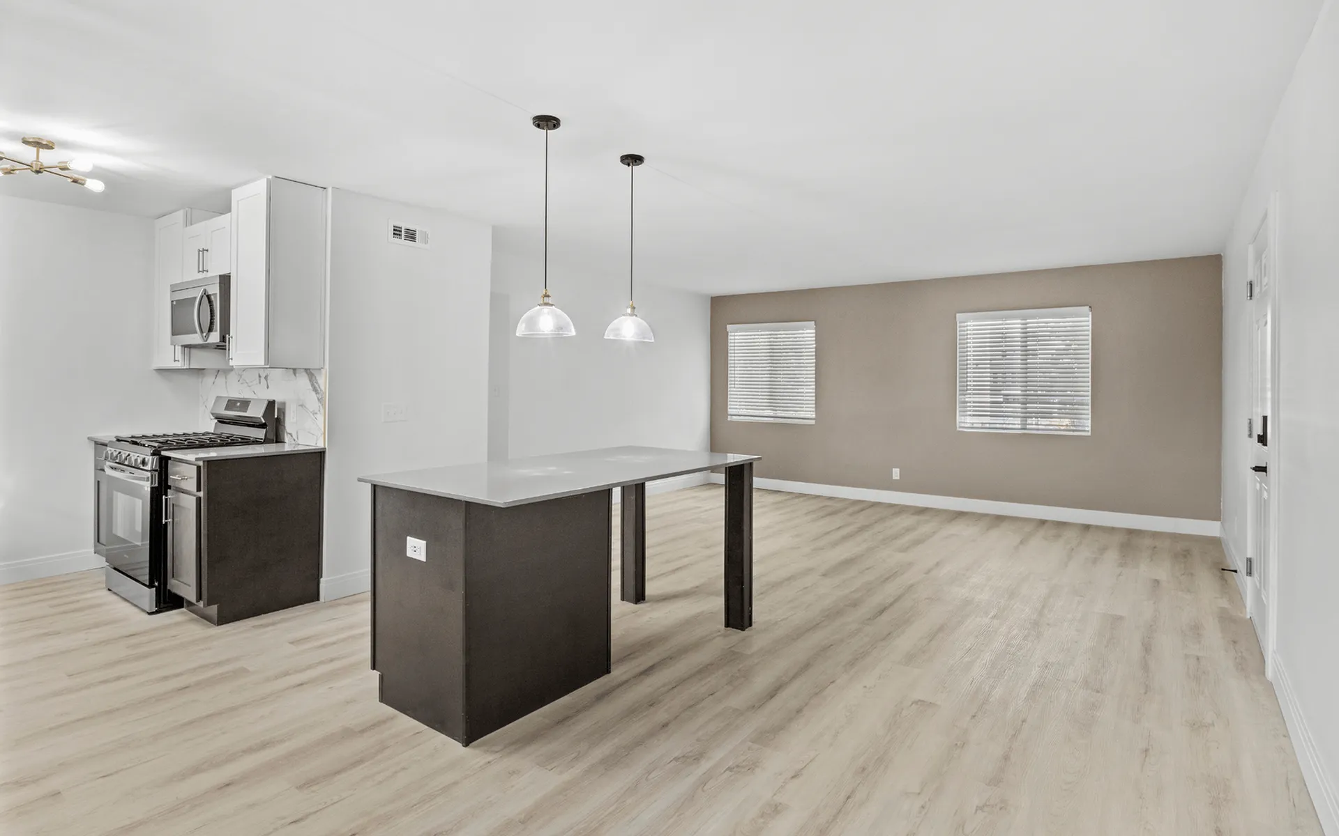 Modern open-concept kitchen and living space featuring sleek pendant lighting, a central island, and a stylish stove with metal finishes.