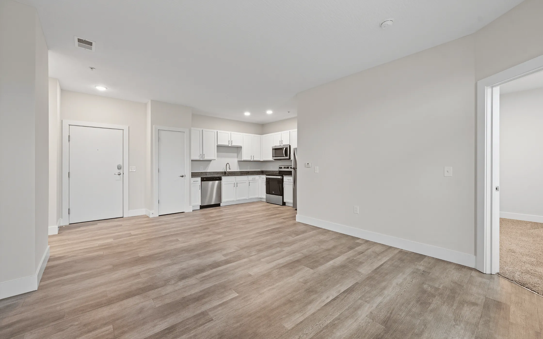 Modern open-concept apartment with warm wood flooring, sleek white cabinetry, and stainless steel appliances in the kitchen.