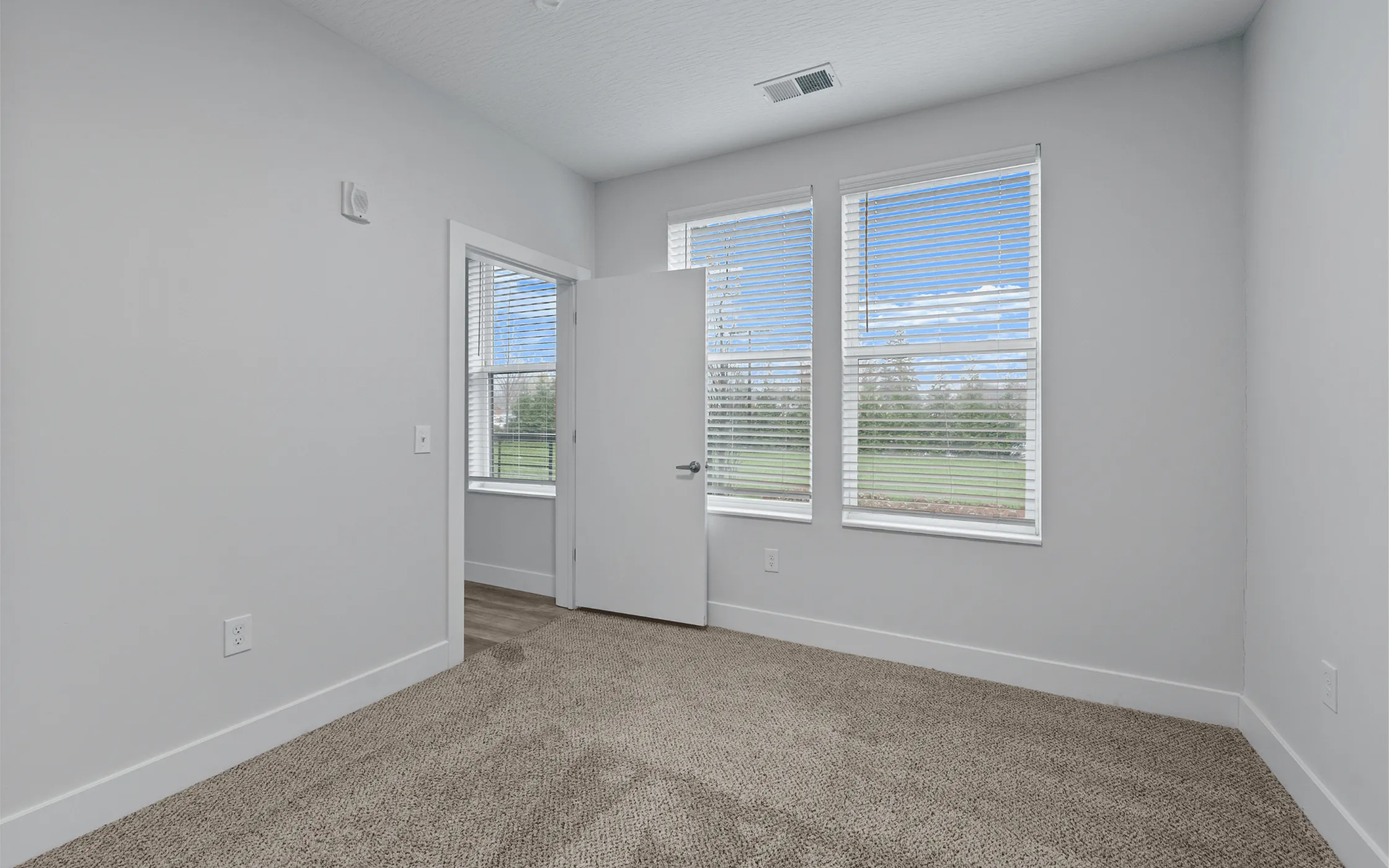 Bright and airy bedroom with large windows, plush carpet, and a door leading to an inviting outdoor view.